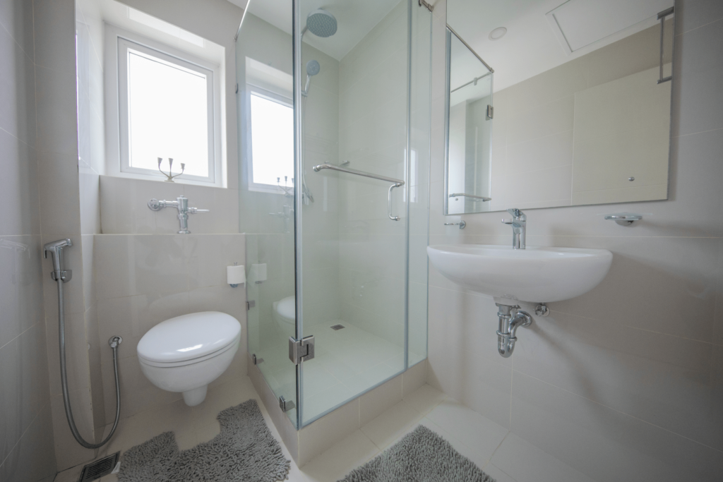 This image shows the shared toilet at Aganthuka villas, which includes a shower and window for natural light. The space is decorated with colourful rugs and a towel rack for convenience.